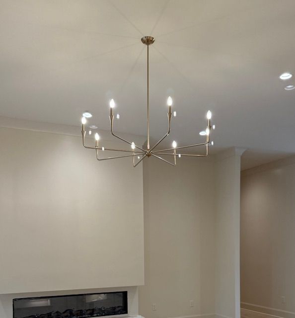Modern gold chandelier with lit bulbs hanging from a beige ceiling in a room