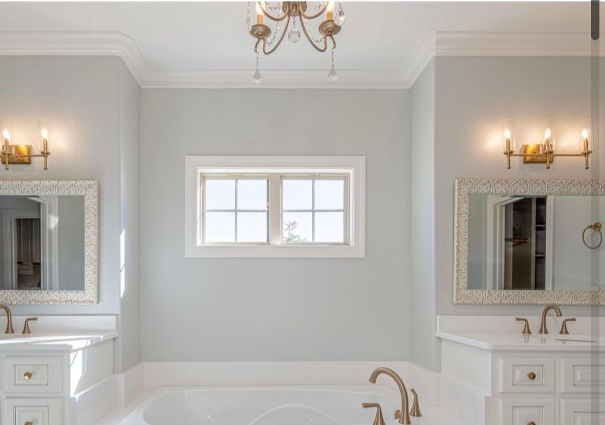 Elegant white bathroom with a soaking tub, double vanities, gold fixtures, and a central window