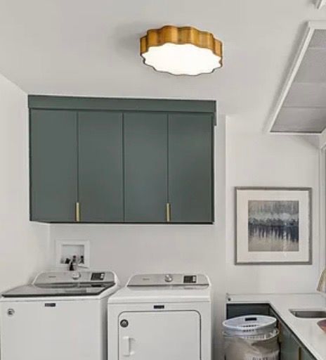 Laundry room with dark green cabinets, white washer and dryer, framed wall art, and a scalloped ceiling light