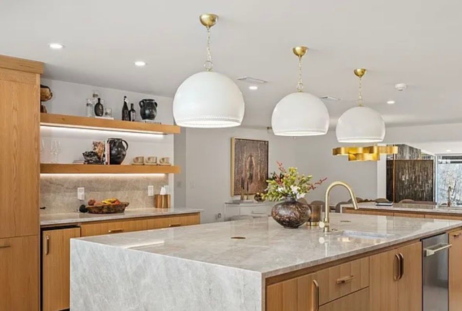 Modern kitchen with a large marble island, wood cabinets, open shelves, and white pendant lights