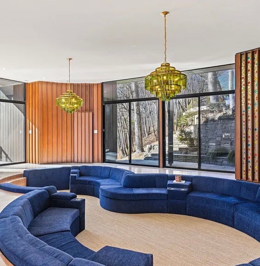 Curved blue seating in a modern lounge with hanging green chandeliers and large windows.