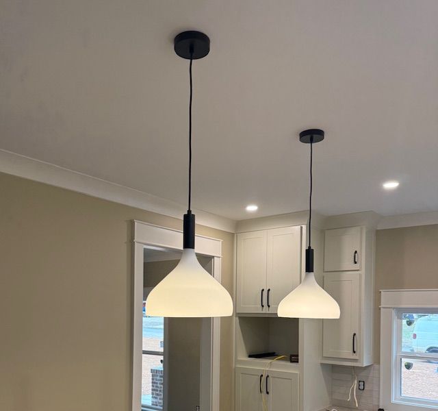 Two white pendant lights hanging over a kitchen with cream cabinets and recessed ceiling lights