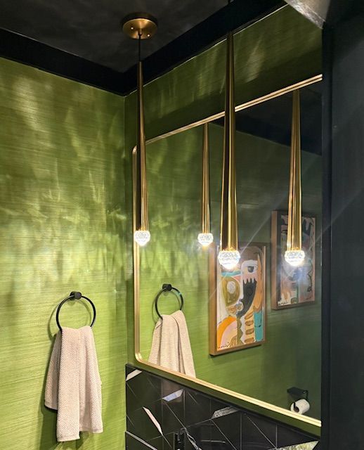 Green bathroom with brass accents, hanging pendant lights, and towels on black towel rings.