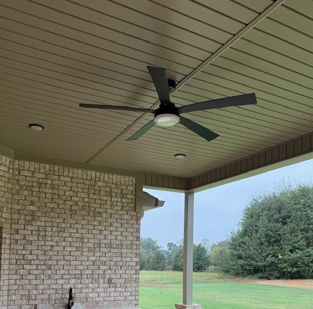 Covered patio with ceiling fan, brick wall, and view of grassy yard and trees