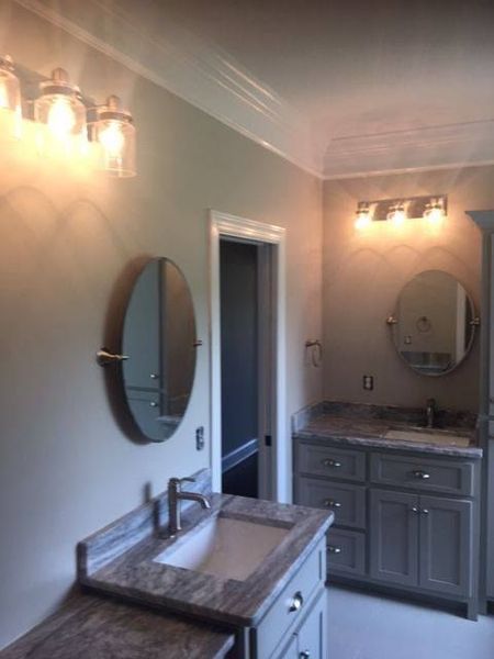 Two elegant bathroom vanities with oval mirrors, stone countertops, and warm wall sconces.