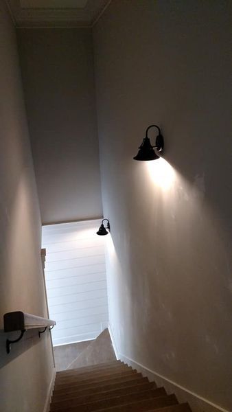 Stairwell with white walls, wooden steps, and two black wall sconces casting light.