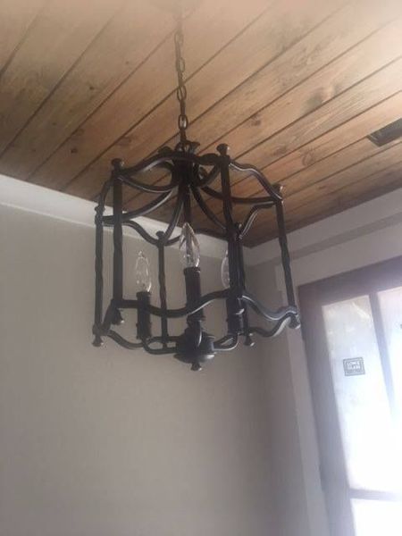 Black wrought-iron chandelier hanging from a wood-paneled ceiling in a room near a window