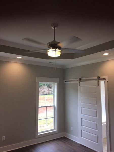Empty gray room with a ceiling fan, recessed lights, window, and white barn-style door.