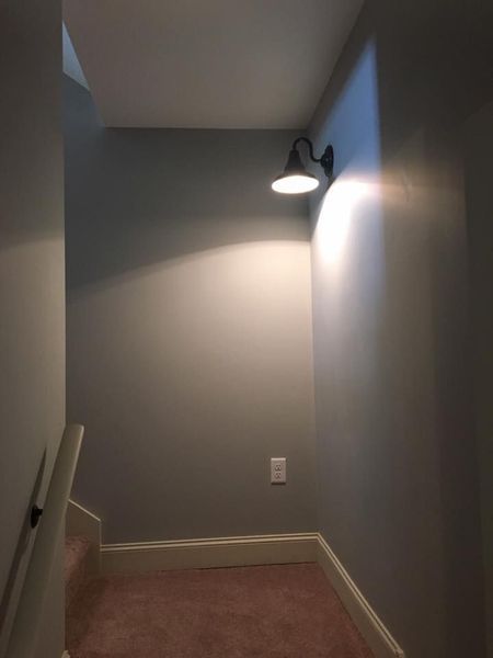 Empty gray hallway with a wall light and beige carpet