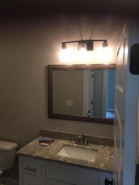 Bathroom vanity with granite countertop, sink, mirror, and wall light above.