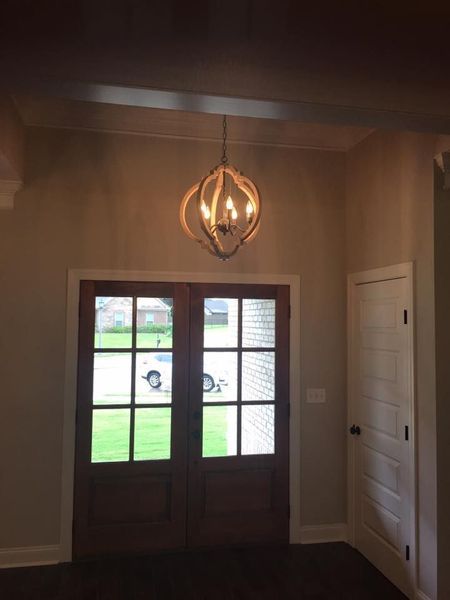 Front entry with wooden double doors, hanging light fixture, and white side door in a beige foyer