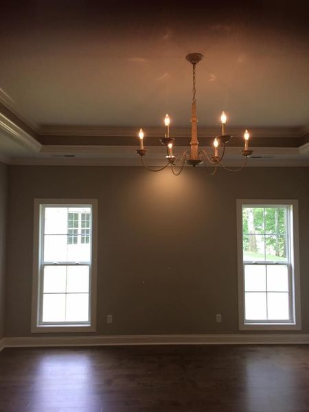 Empty dining room with chandelier, beige walls, dark wood floor, and two windows.