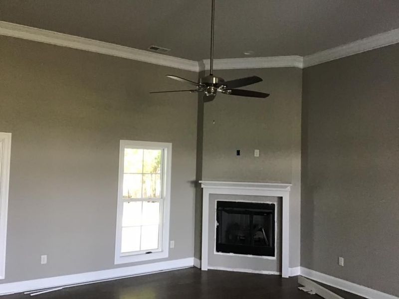 Empty living room with gray walls, white trim, a fireplace, a window, and a ceiling fan.