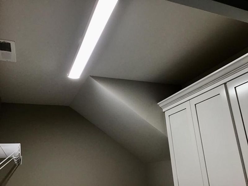 Ceiling corner with a bright linear light and white cabinets against gray walls.