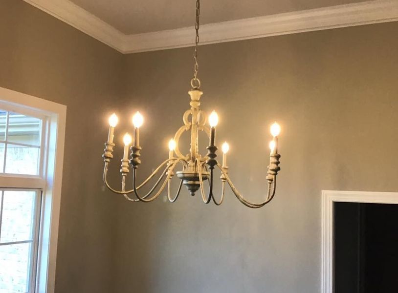 Brass chandelier with lit bulbs hanging in a beige room near a window and doorway.
