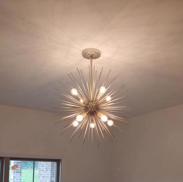 Modern starburst chandelier with lit bulbs hanging from a white ceiling above a room window