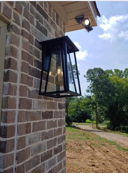 Black metal lantern on a brick wall beside a dirt path and trees outdoors