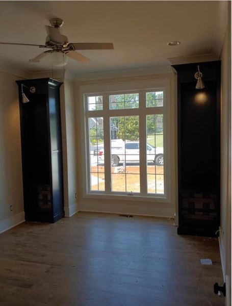 Empty room with wood floor, ceiling fan, and large window with black cabinets on both sides.