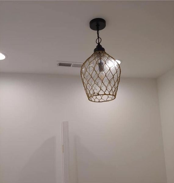 Wire cage pendant light hanging from a white ceiling in a minimal room.