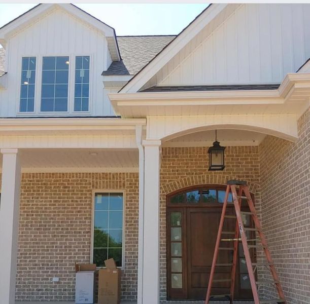 Front porch of a brick house with white trim and a red ladder leaning near the front door.
