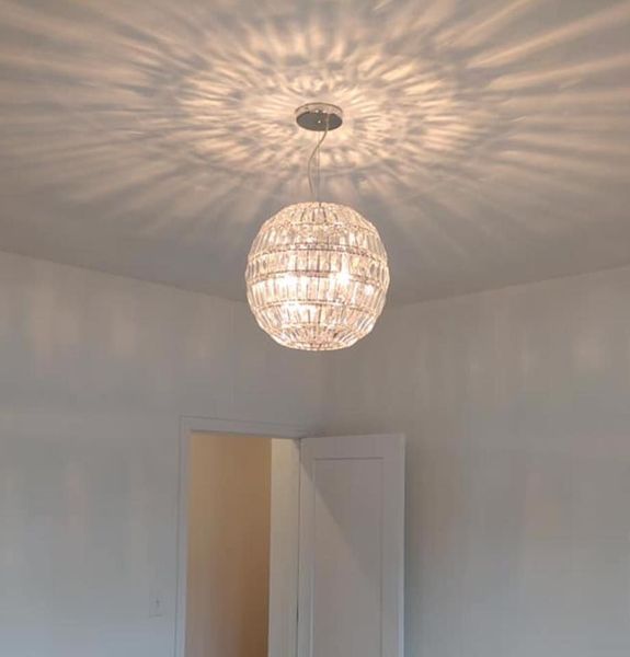 White room with a woven pendant light casting a patterned shadow on the ceiling above an open door.