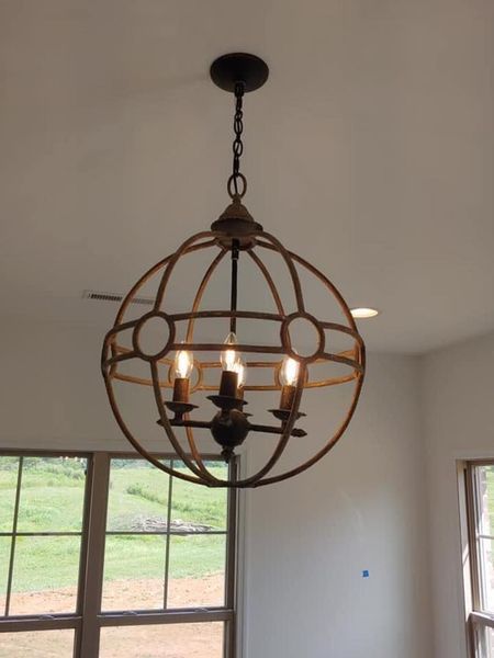Rust-colored spherical chandelier with lit bulbs hanging in a bright room near windows