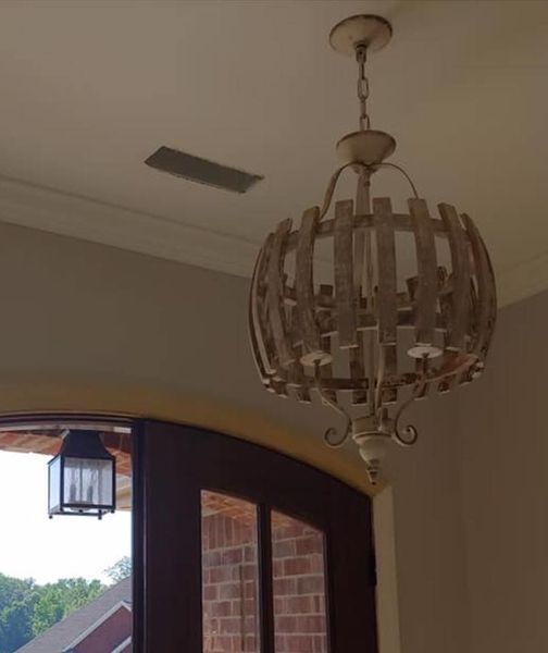 Wooden chandelier hanging from a ceiling above an arched doorway with brick walls and a small outdoor lantern visible.