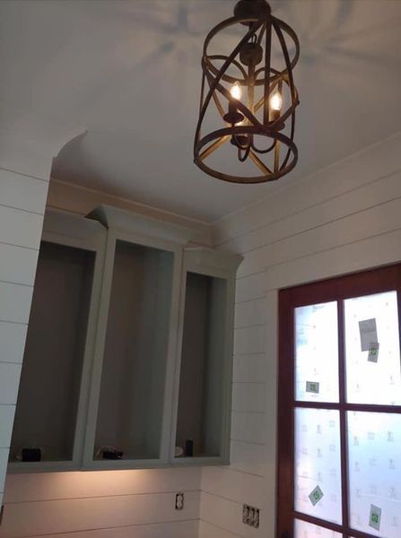 Empty room with white shiplap walls, hanging metal light fixture, and a window with frosted panes