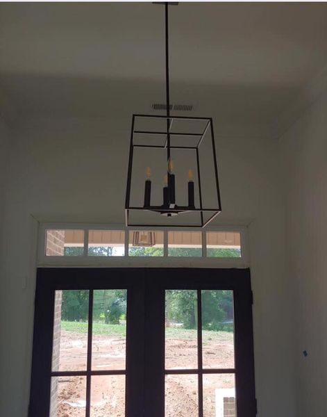 Black metal chandelier hanging in front of a windowed door in a dim room
