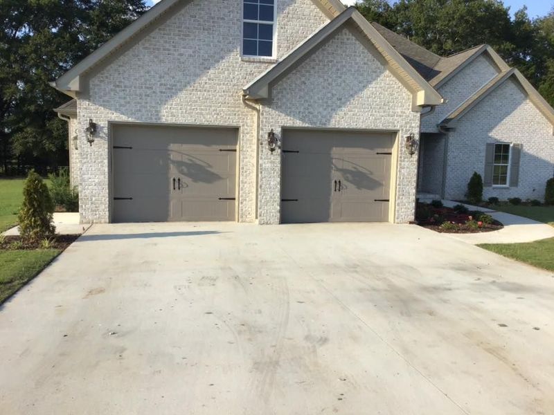 Two gray garage doors on a light brick house with a wide concrete driveway in front.
