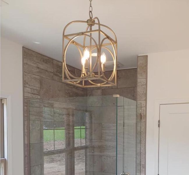 Gold geometric pendant light over a glass shower enclosure in a tiled bathroom