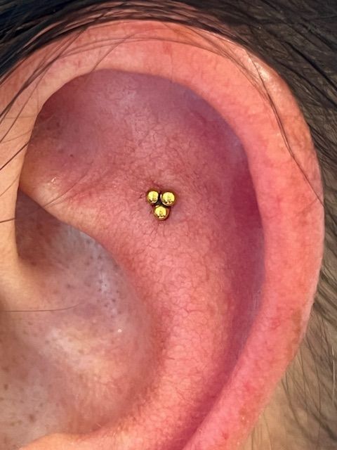 Een close-up van een menselijk oor met een kleine, gouden, driehoekige clusterpiercing op het platte gedeelte.