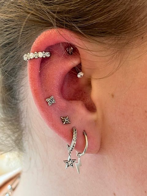 Een close-up van een oor versierd met meerdere zilveren piercings, waaronder ringen, oorstekers en een helixpiercing bezet met edelstenen.