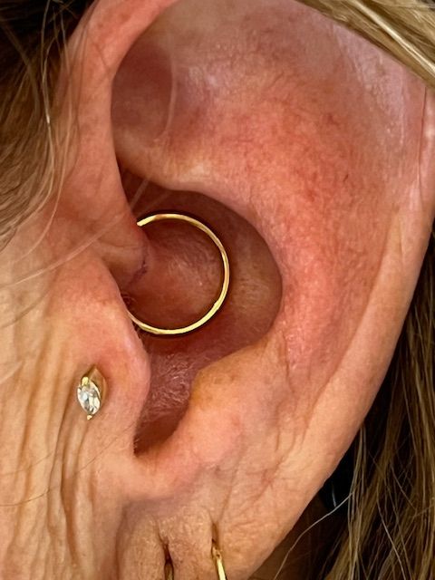 Een close-up van een menselijk oor met een gouden daith-piercing en een klein, marquise-geslepen oorknopje in de tragus.