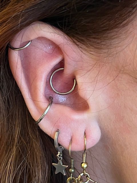Close-up van een oor met een helix-, daith-, conch- en drie oorlel-piercings, versierd met metalen oorringen.
