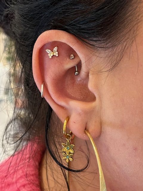 Close-up van een oor met meerdere goudkleurige piercings, waaronder een vlinderpiercing en een rookpiercing.