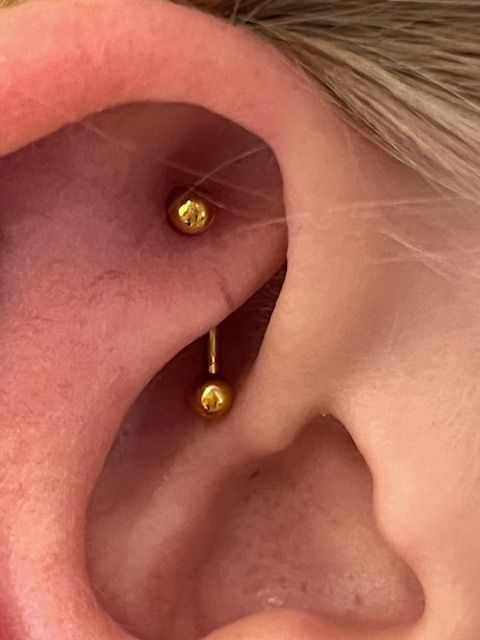 Een close-up van een gouden gebogen barbell-piercing in de rook van een oor.