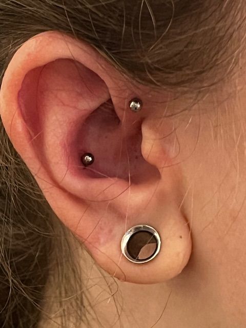 Het oor van een persoon met een zilveren sieraad in de oorlel en een rookpiercing met twee metalen balletjes.