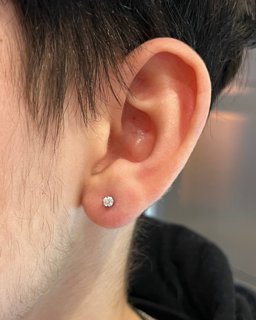 Een close-up van een oorlel met een enkel, klein, glinsterend oorknopje.