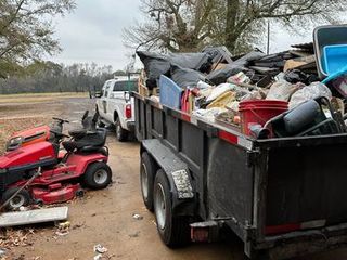 A dumpster filled with trash is parked next to a lawn mower.