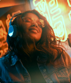 a woman wearing headphones and sunglasses is smiling in front of a neon sign .