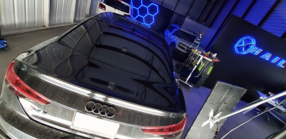 A high-angle view of a grey Audi parked inside a garage with blue hexagonal LED lighting and a signage wall.