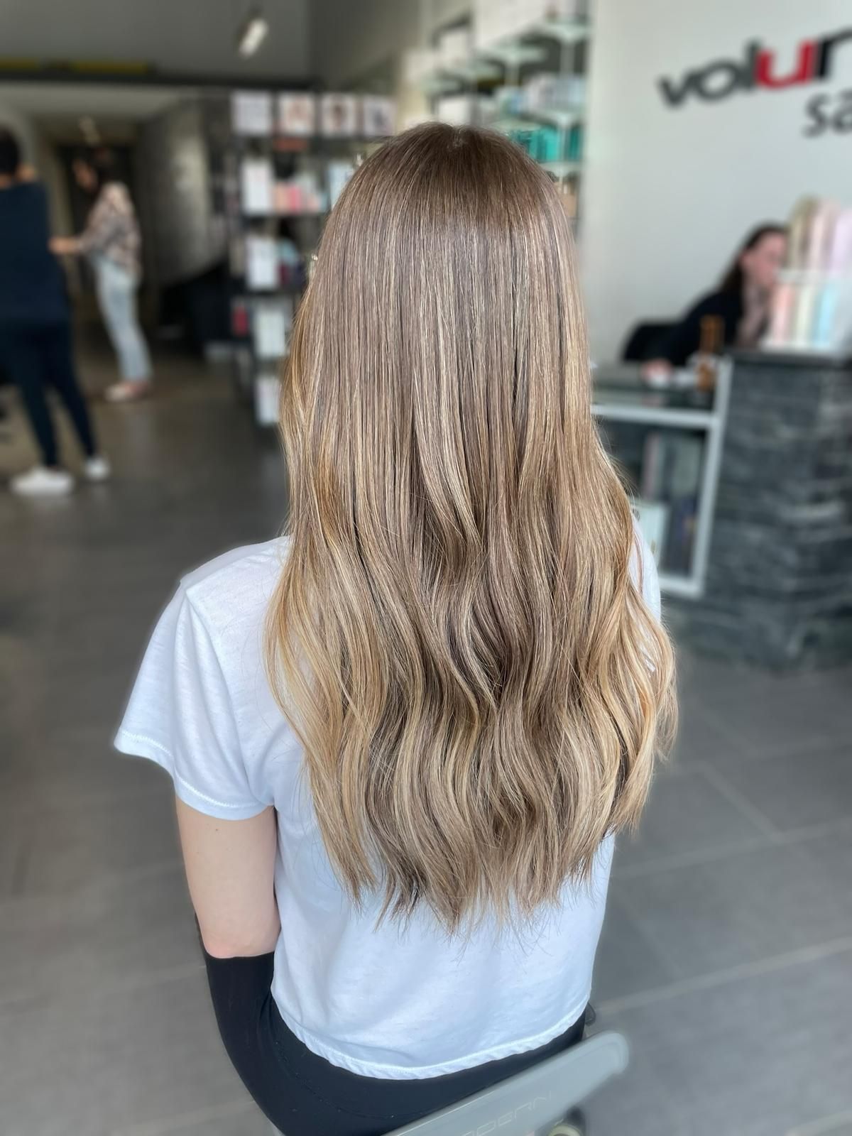 A woman with long hair is sitting on a stool in a salon.