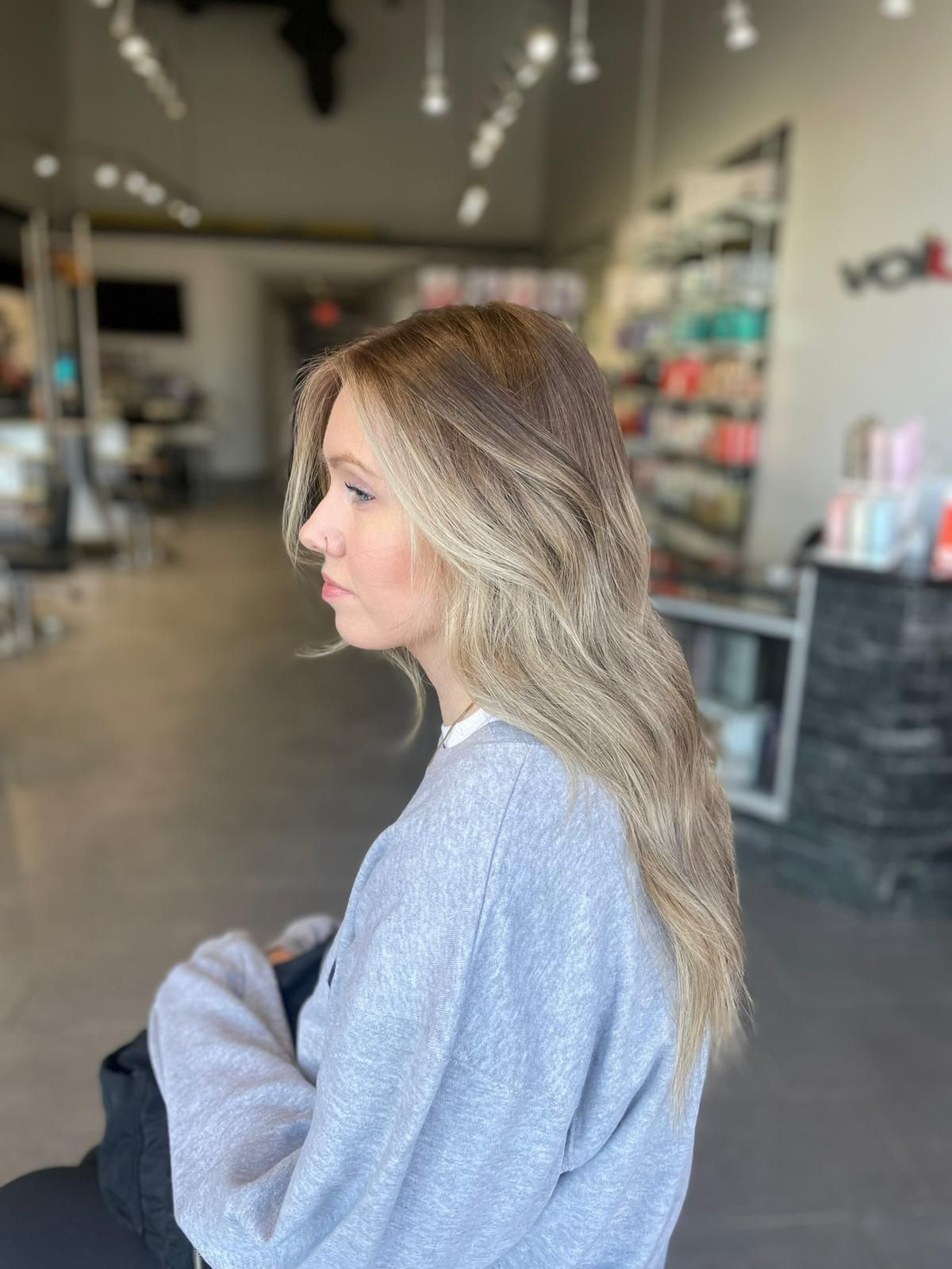 A woman with long blonde hair is sitting in a chair in a salon.