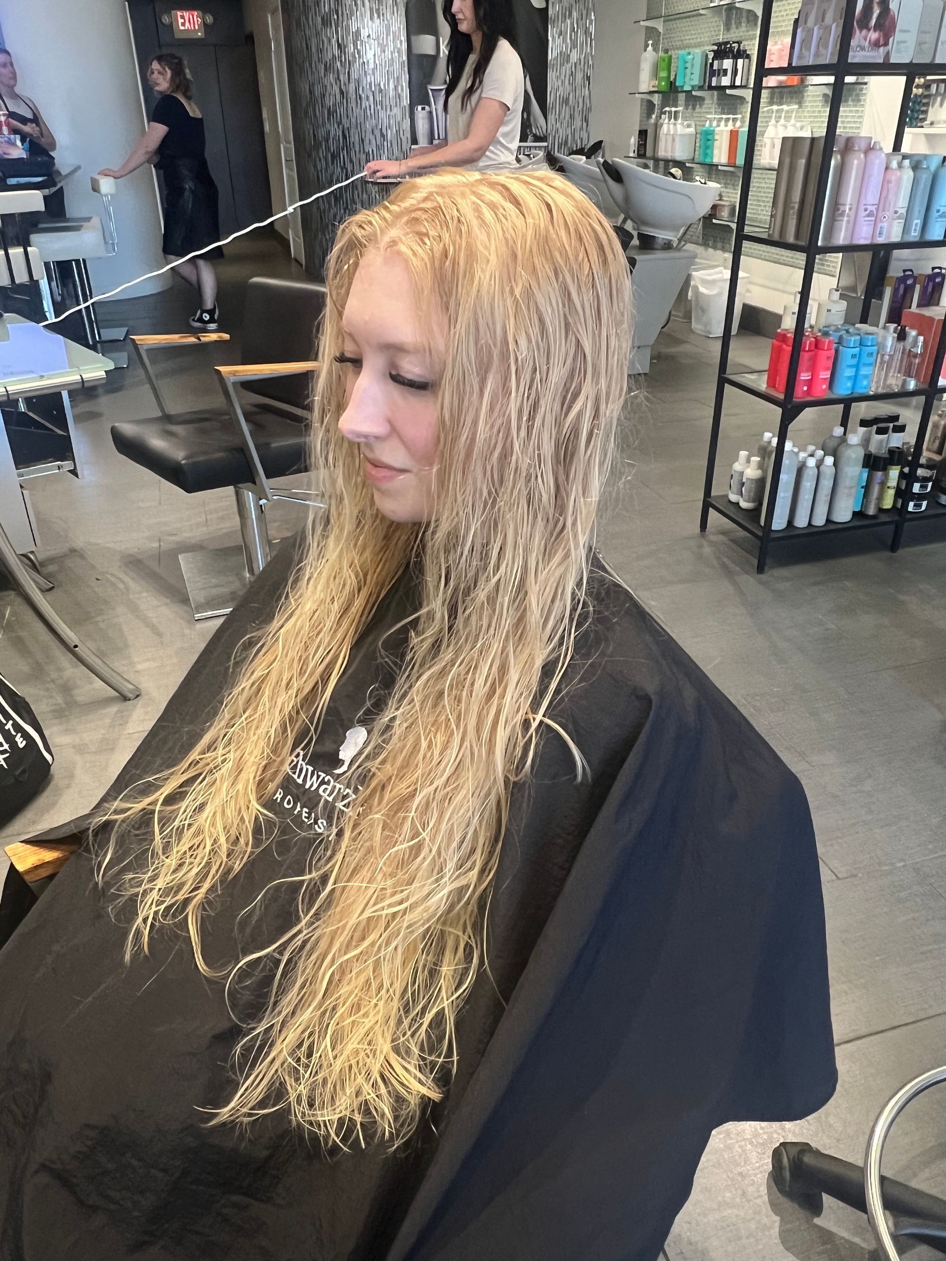 A woman with long blonde hair is getting her hair cut in a salon.