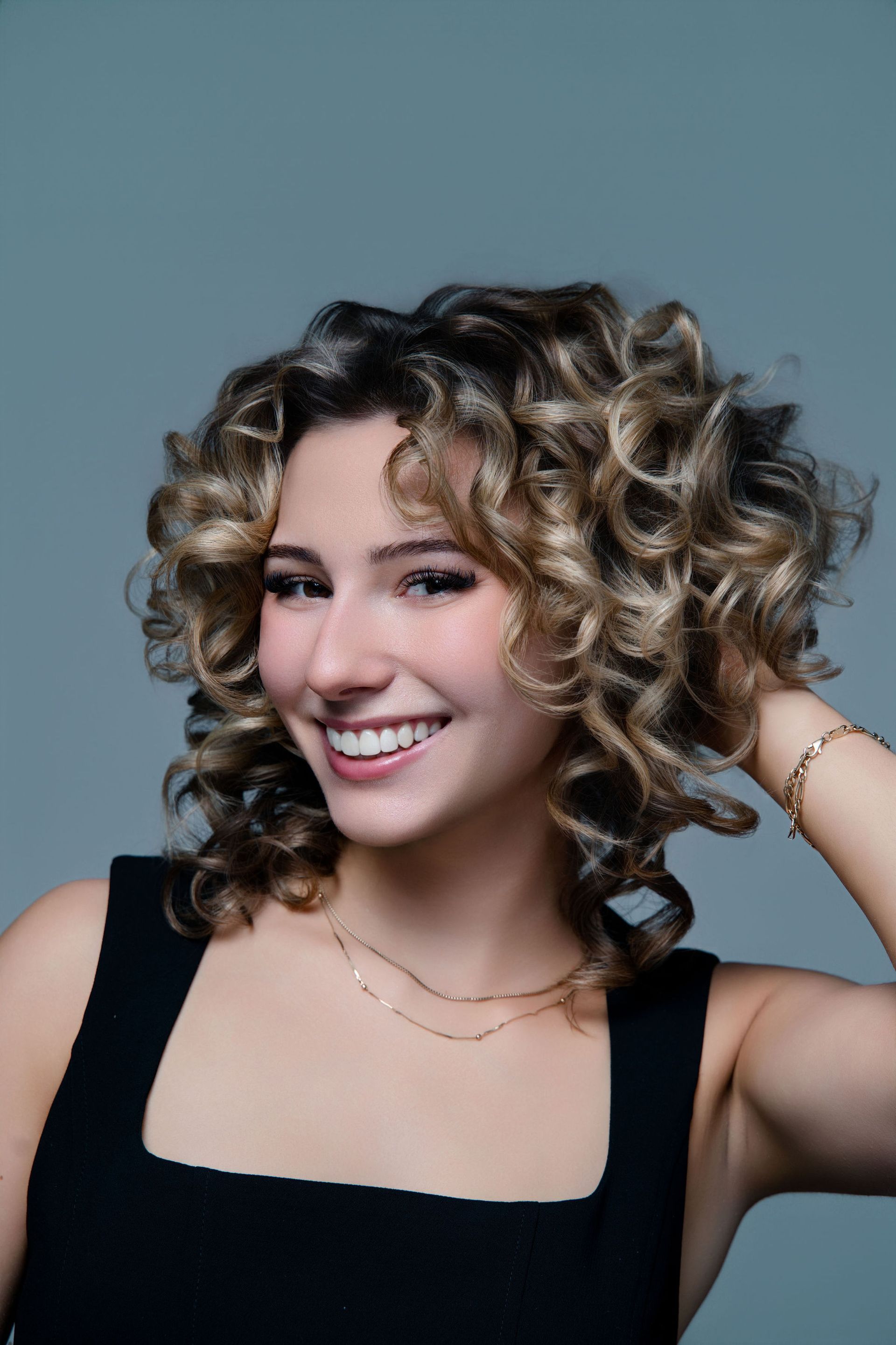 A woman with curly hair is wearing a black tank top and smiling.
