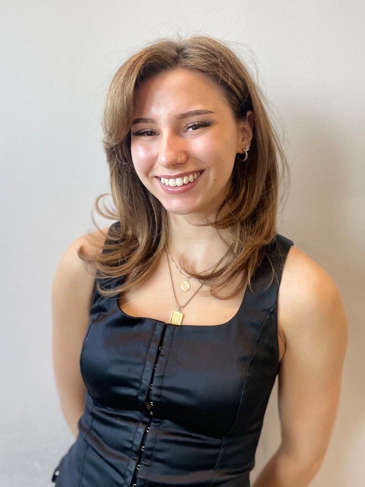 A woman in a black tank top is smiling and wearing a necklace.