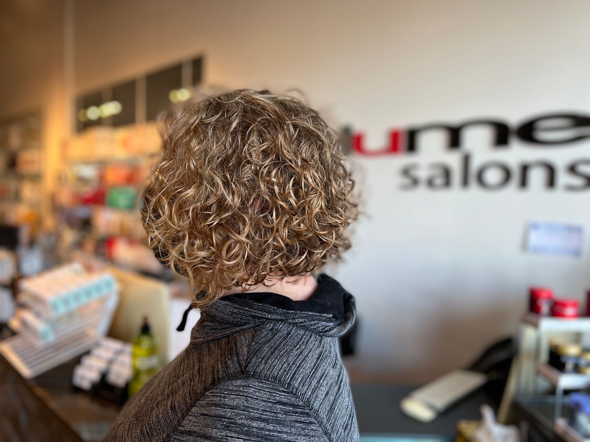 A woman with curly hair is standing in front of a sign that says salons.