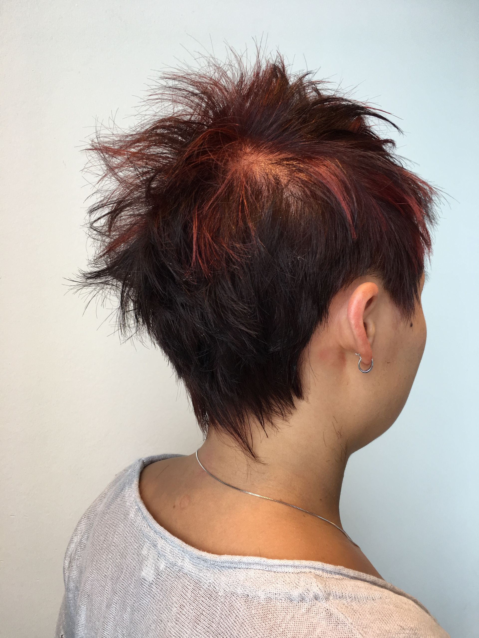 A woman with short red hair is wearing a white shirt and earrings.