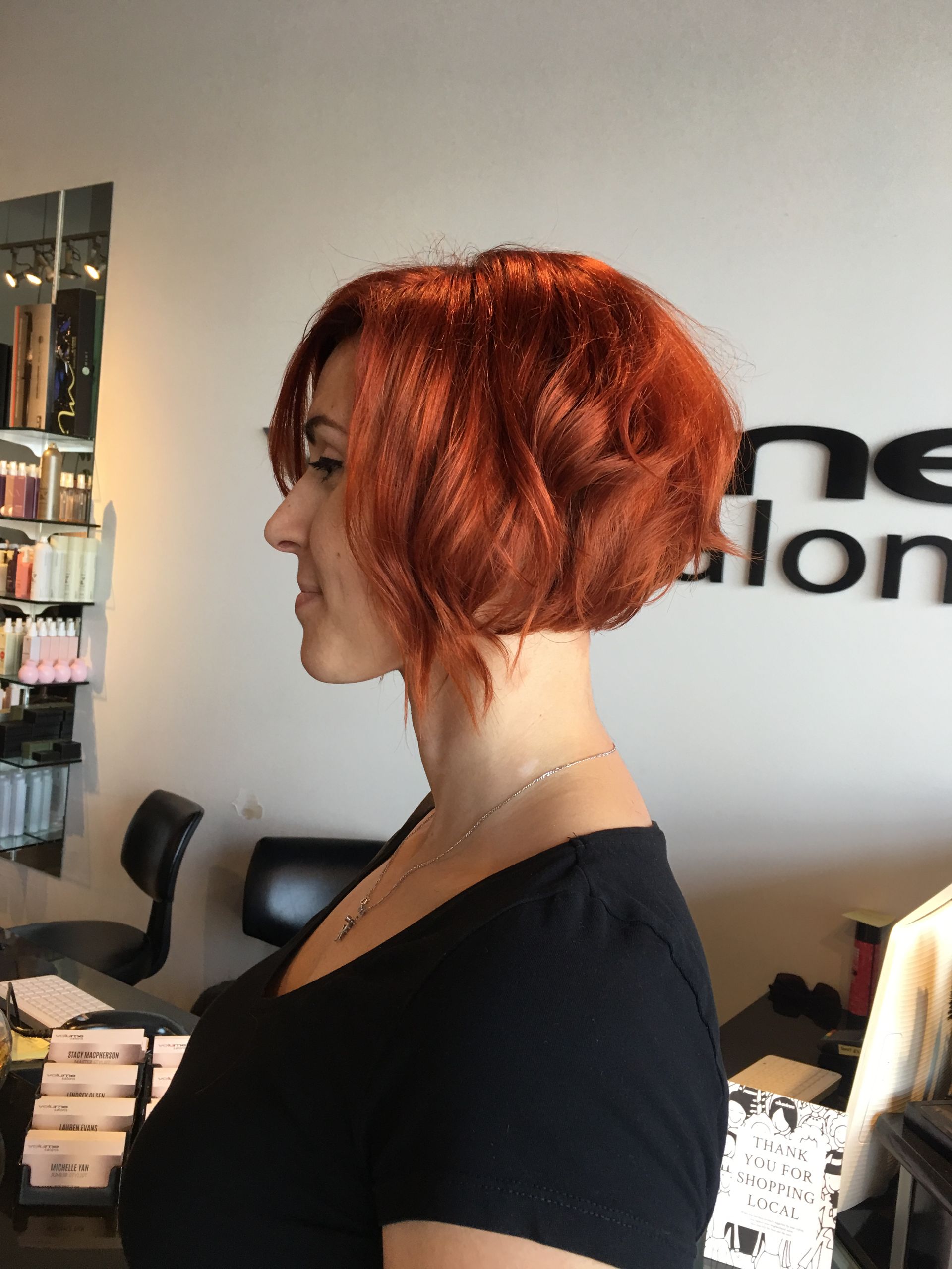 A woman with red hair is standing in front of a salon sign